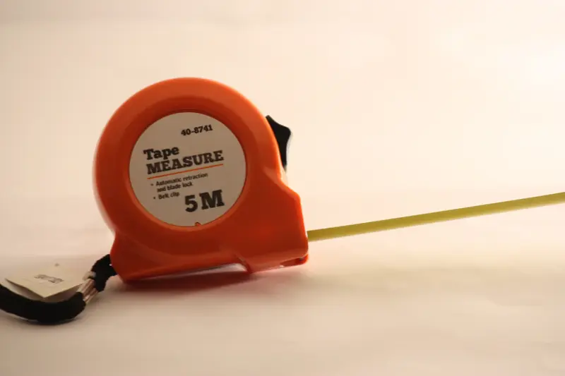 An orange tape measure with its yellow blade pulled out across a white surface